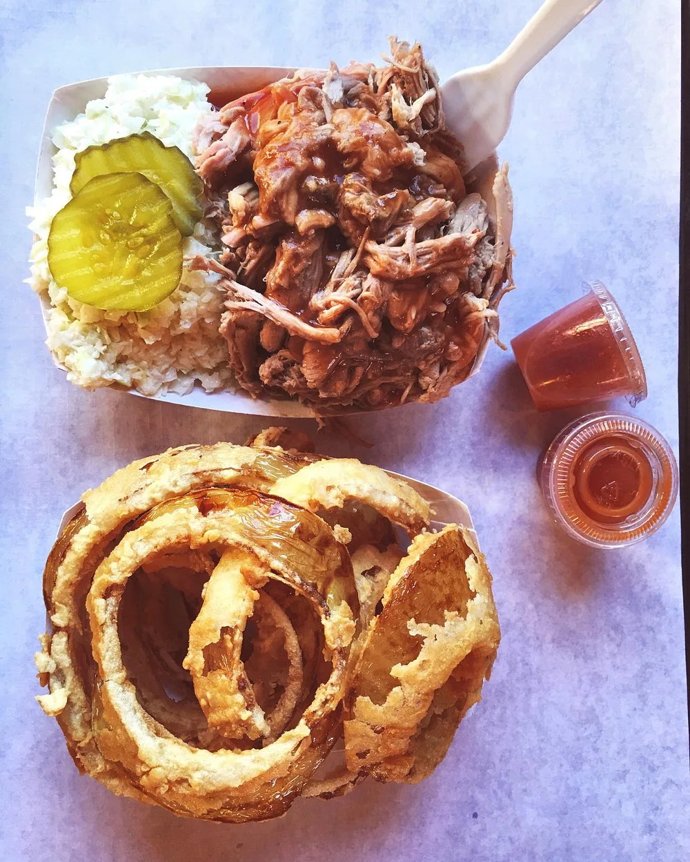 Tray of hand-breaded onion rings and a pulled pork plate with pickles and slaw on a wood tabletop