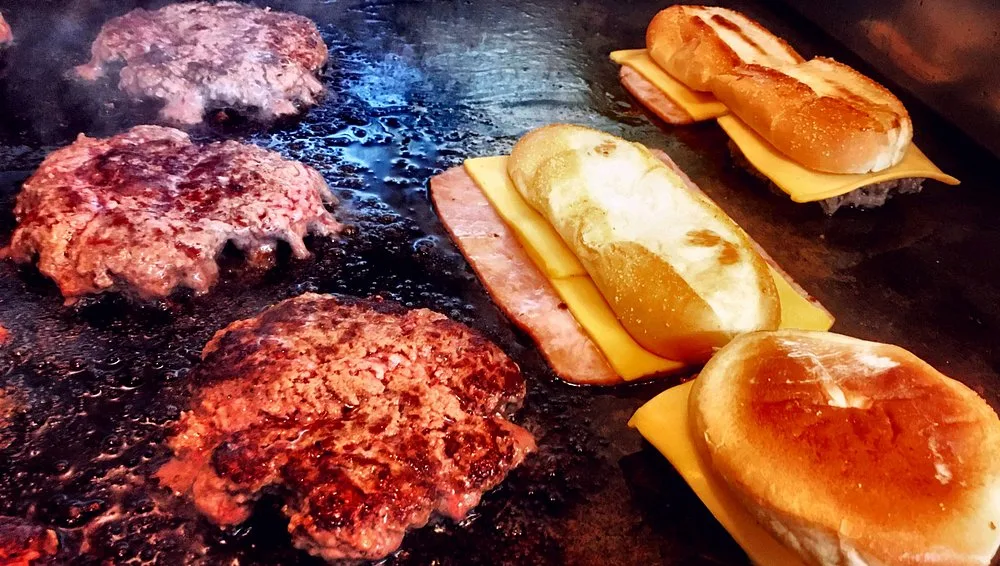 Burgers and ham sandwiches with melted cheese cooking together on the hot griddle
