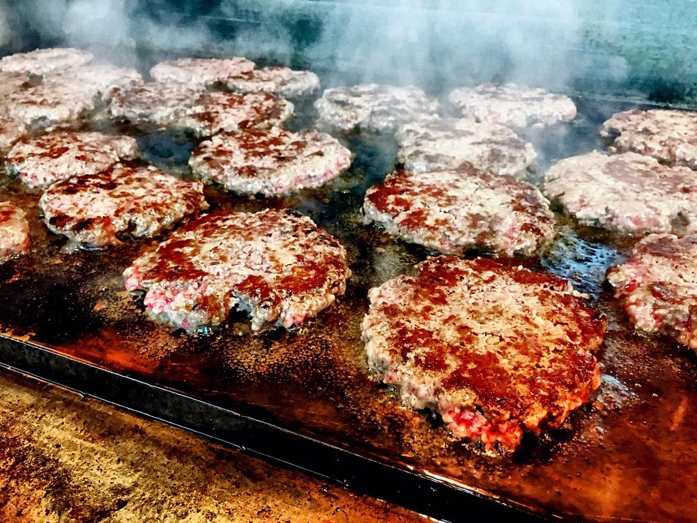 Hand-pattied hamburgers sizzling on BBQ King's flat-top grill with rising steam