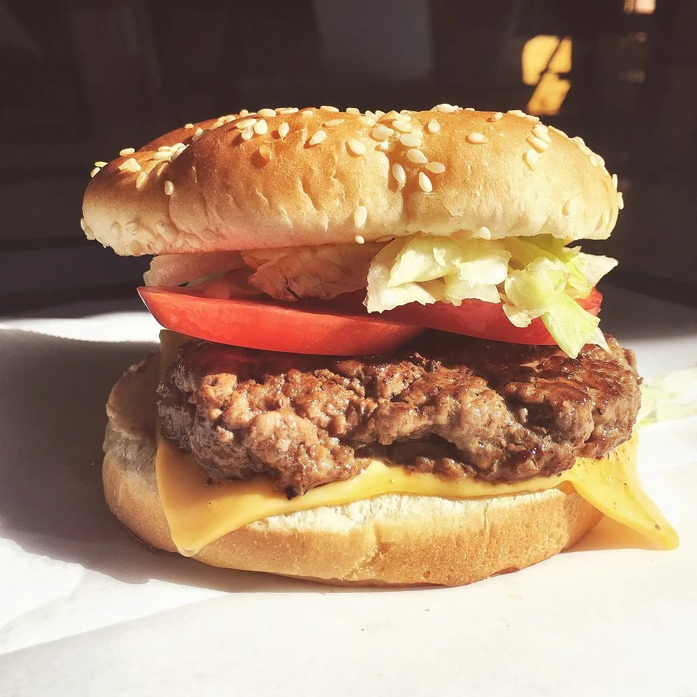 Close-up of a hand-pattied cheeseburger with lettuce and tomato in bright sunlight