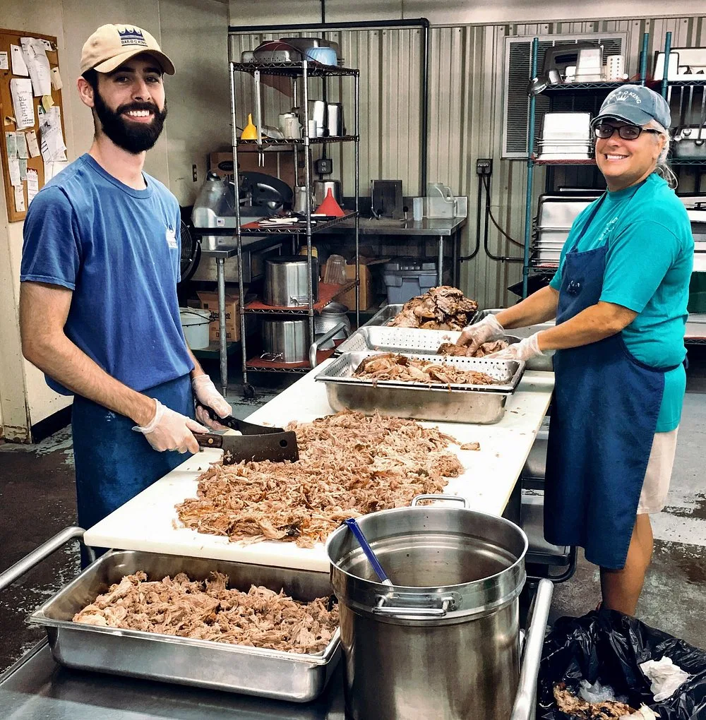 A BBQ King employee and coworker pausing from chopping pork to smile for a photo