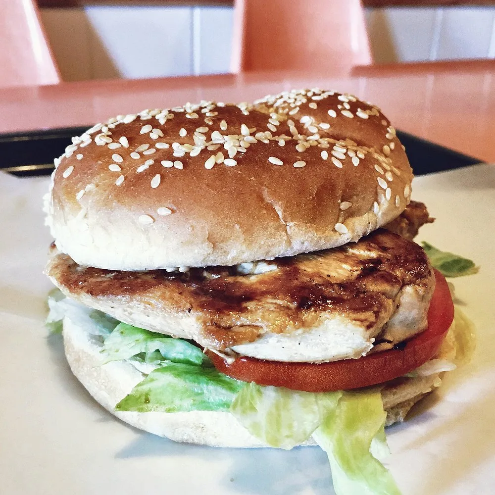 Grilled chicken sandwich with lettuce and tomato served beside a basket of onion rings