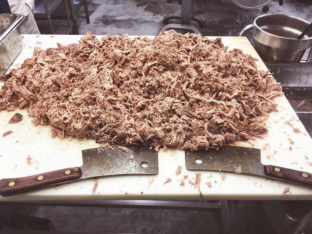 Mound of hand-chopped pork shoulder on a cutting board with two cleavers, fresh off the pit