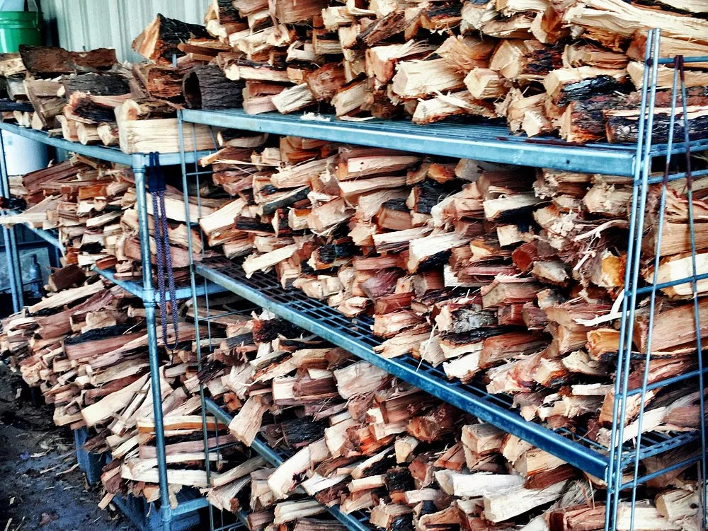 Rows of hickory firewood stacked deep on wire shelving in BBQ King's wood shed