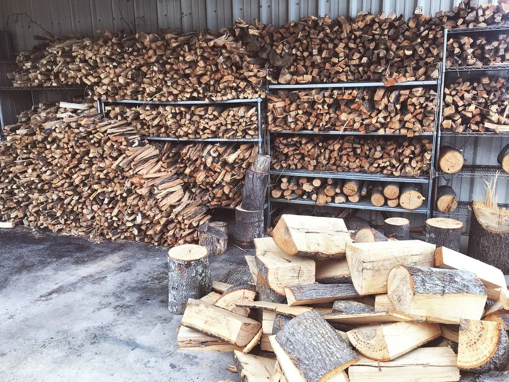 Split hickory logs and cut stumps stacked on metal shelving, ready to feed the pit