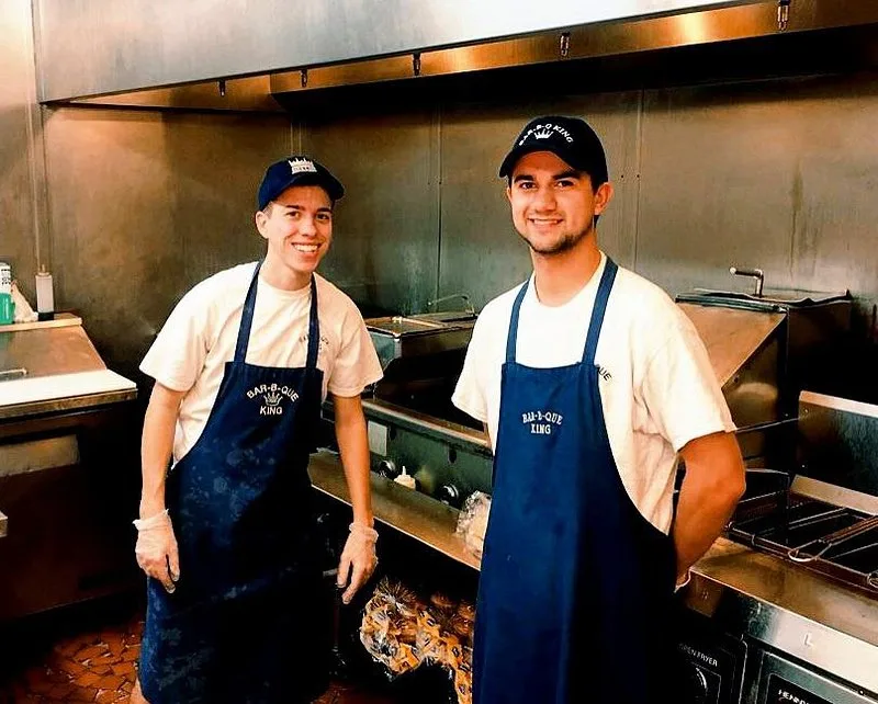 Jordan and Jared Smith standing together in the kitchen in matching Bar-B-Q King aprons