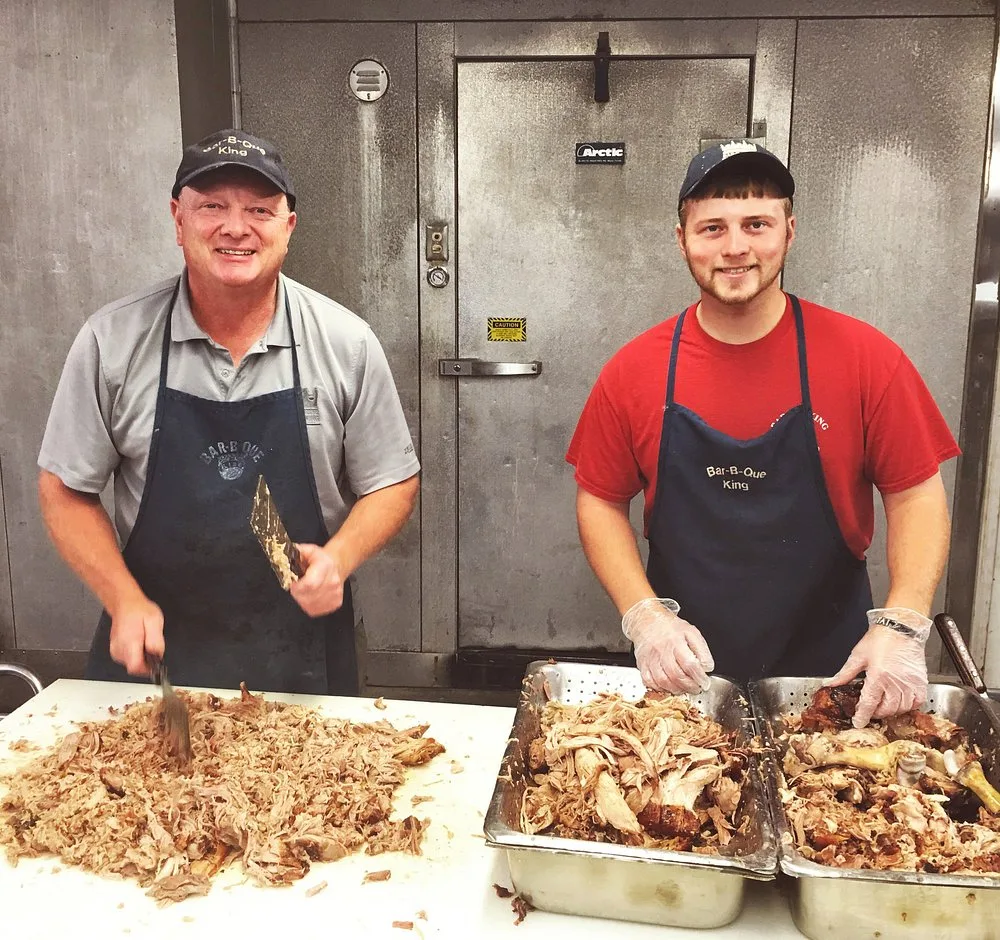 Keith Smith and a young employee hand chopping pulled pork on stainless steel prep tables