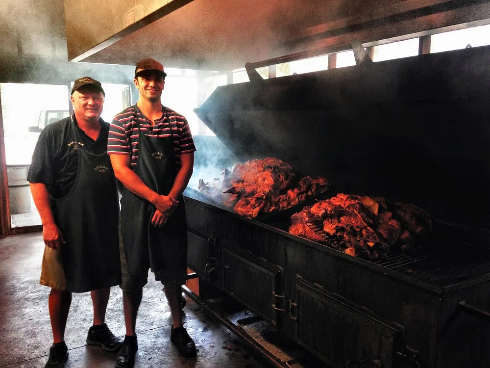 Keith Smith and his son Jordan posed beside the open pit, smoked meat visible behind them