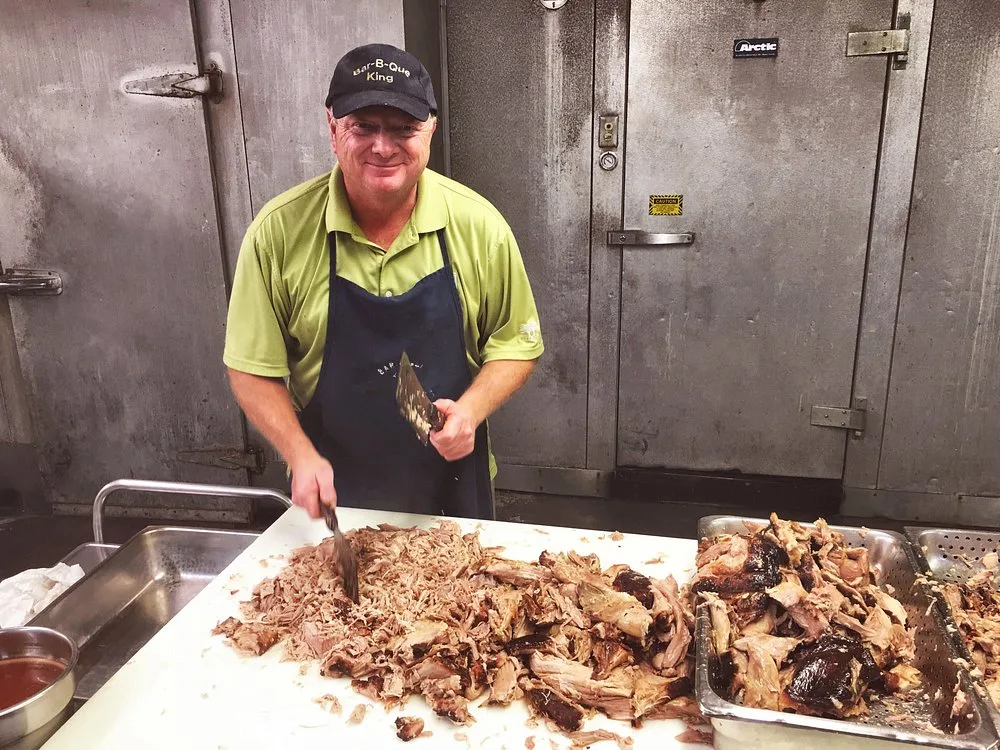 Keith Smith hand chopping pork shoulder with a cleaver in front of the walk-in coolers