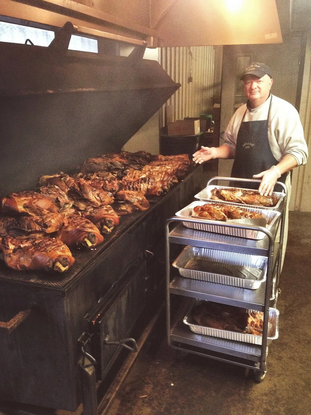 Keith Smith loading smoked pork shoulders onto a cart beside the open pit smoker