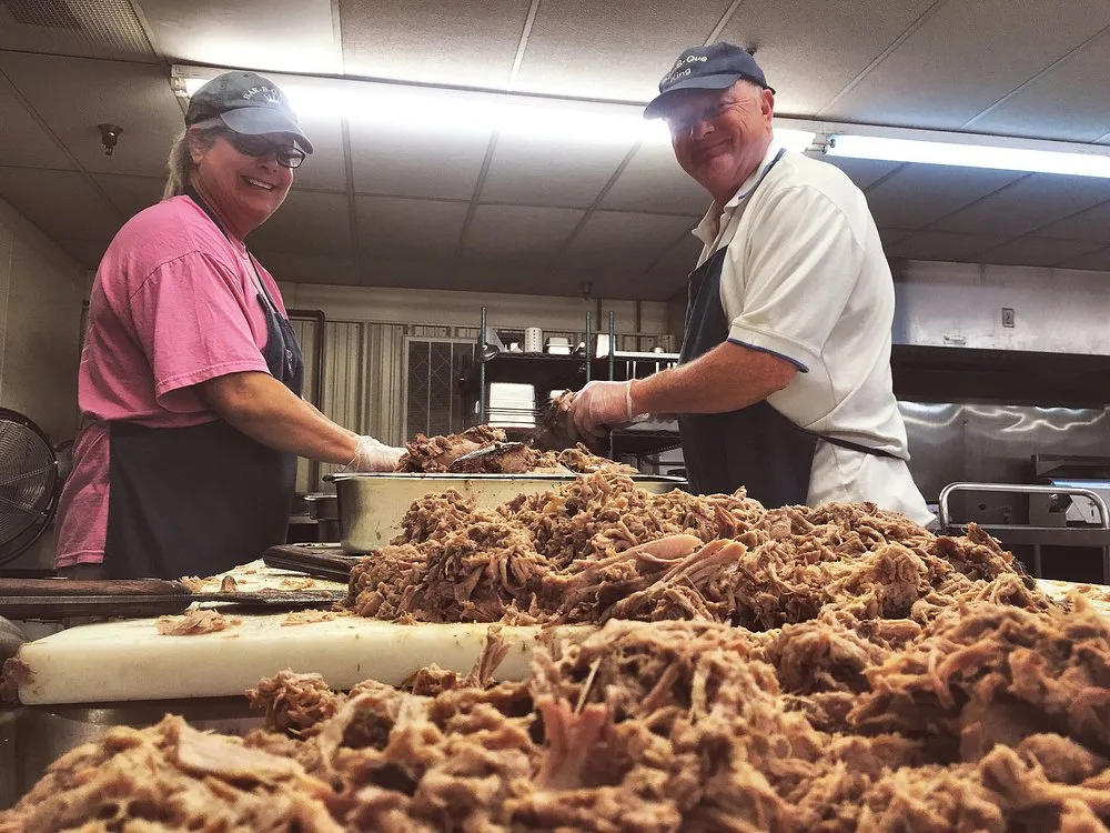 Kelly and Keith Smith smiling while pulling pork together at the prep table