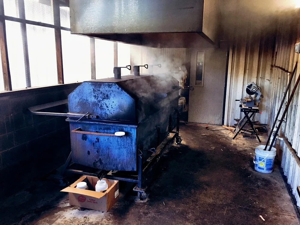 The blue steel pit smoker inside BBQ King's smokehouse, wisps of smoke rising from the firebox doors