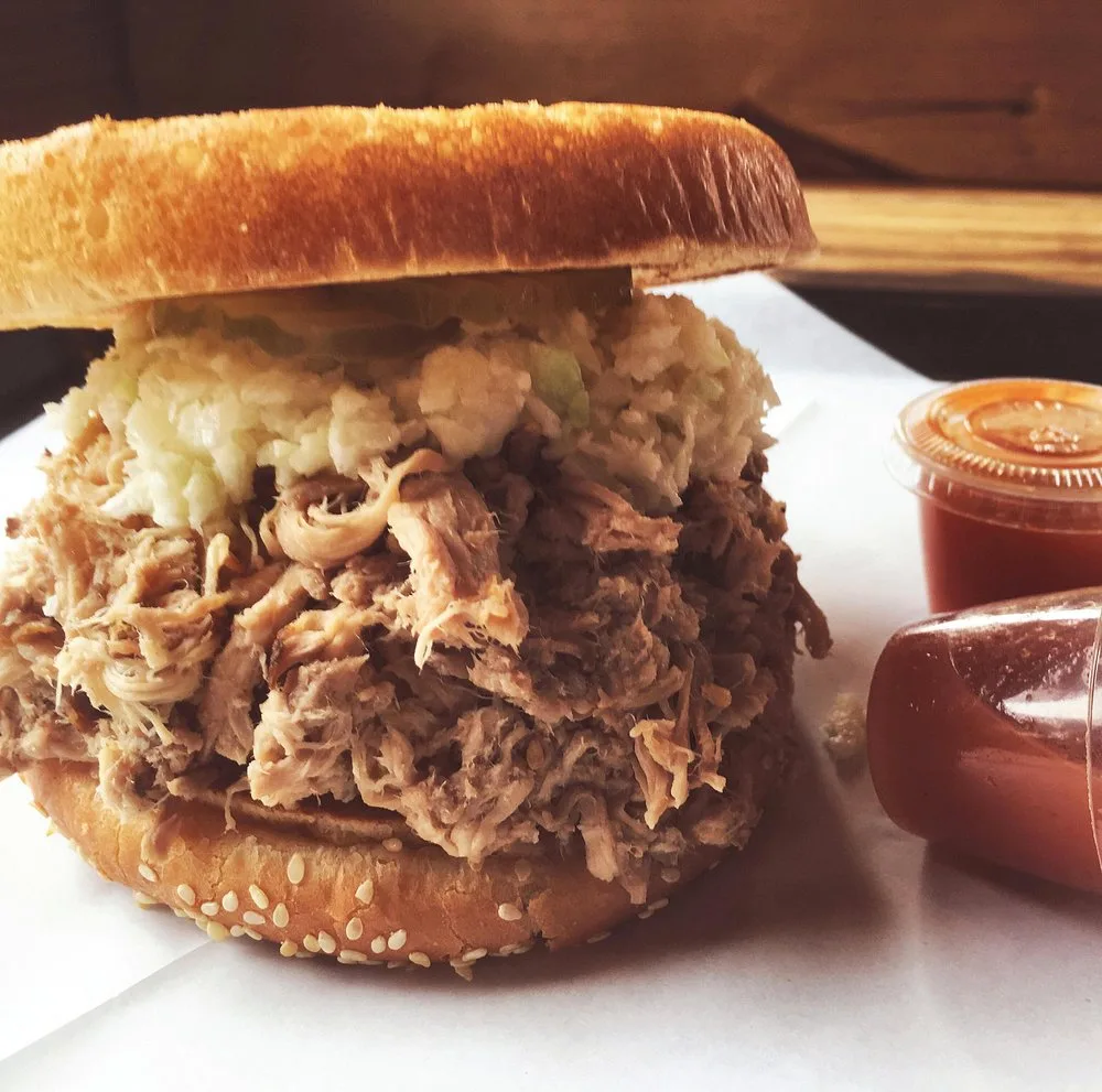Pulled pork sandwich with slaw served with BBQ King's signature sauce on the side in small cups