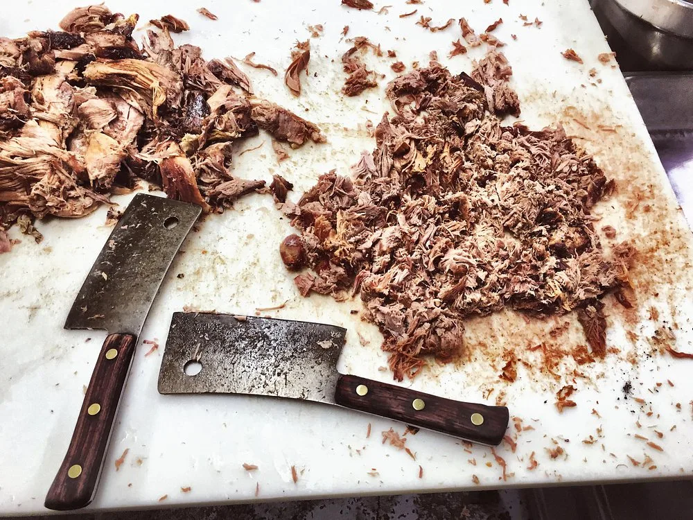 Row of whole pork shoulders fresh off the pit, hickory smoked and ready to be hand chopped