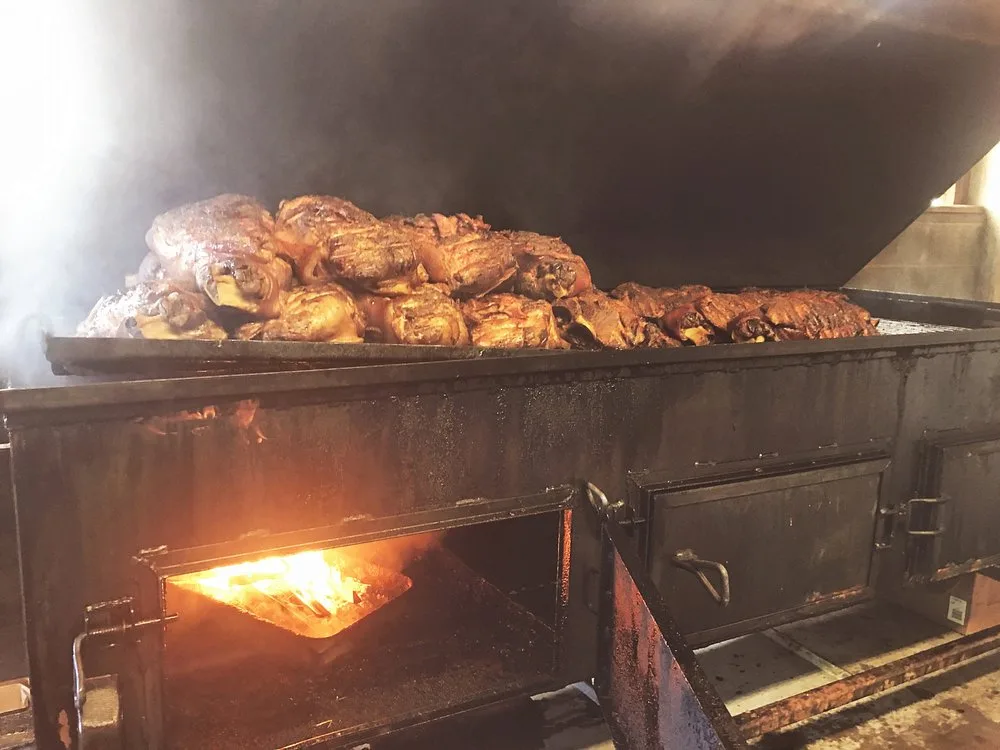 Close view of pork shoulders and chicken pieces on the smoker grate with heavy smoke rolling off them