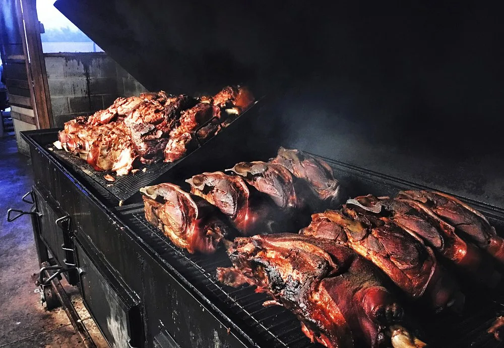 Pit-smoked pork shoulders with a dark, charred bark cooking low and slow on the smoker