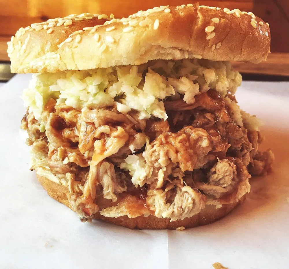 Pulled pork BBQ sandwich topped with slaw on a sesame seed bun