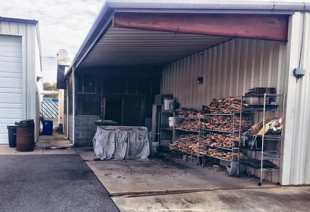 Exterior view of BBQ King's smokehouse with racks of split hickory wood stacked and ready for the pit