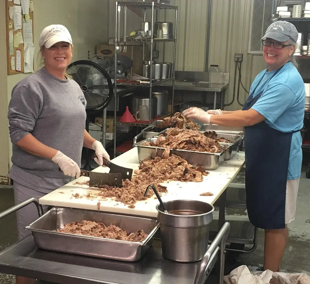 Two BBQ King employees, Stephanie and Kelly, hand pulling a large batch of pork shoulder